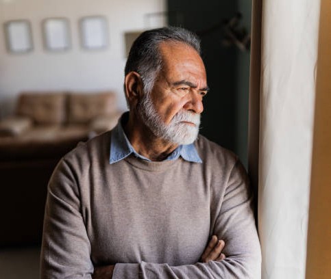 A man in his sixties standing at a window, considering what comes next