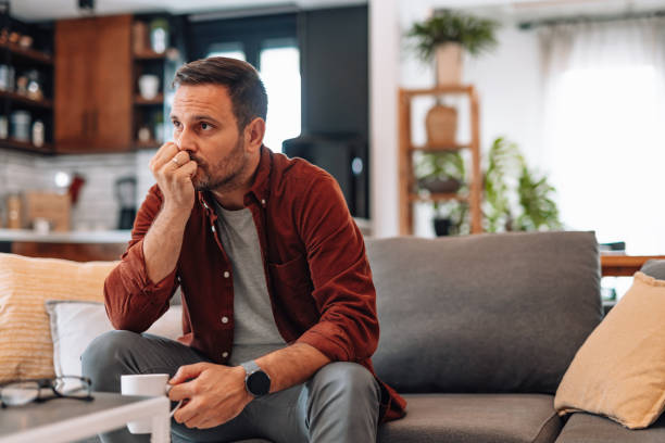 A man in his forties sitting quietly at home with a coffee, thinking things through
